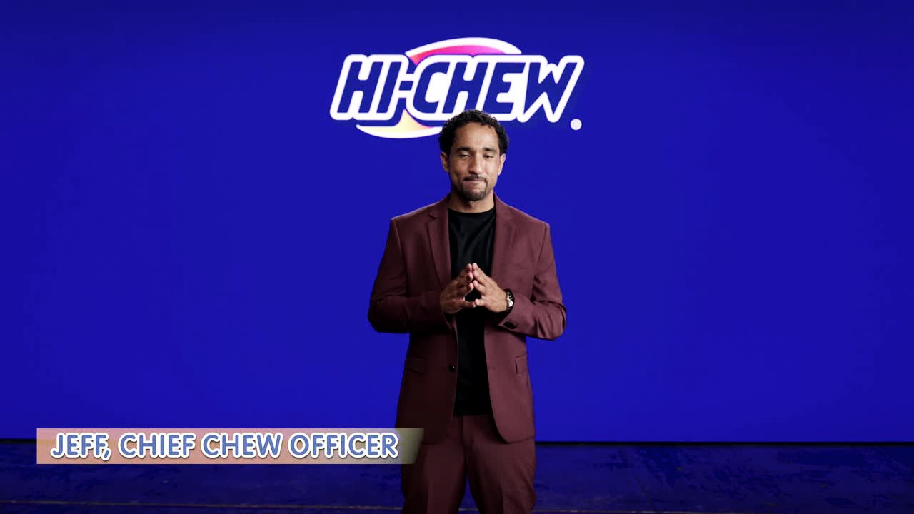 A presenter in a burgundy suit against a bold blue backdrop — the acting reel cover still